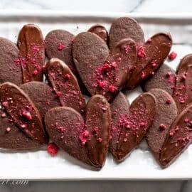 A tray of chocolate Valentine's Day Cookies dipped in dark chocolate and sprinkled with freeze dried raspberries.