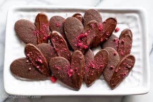A tray of chocolate Valentine's Day Cookies dipped in dark chocolate and sprinkled with freeze dried raspberries.