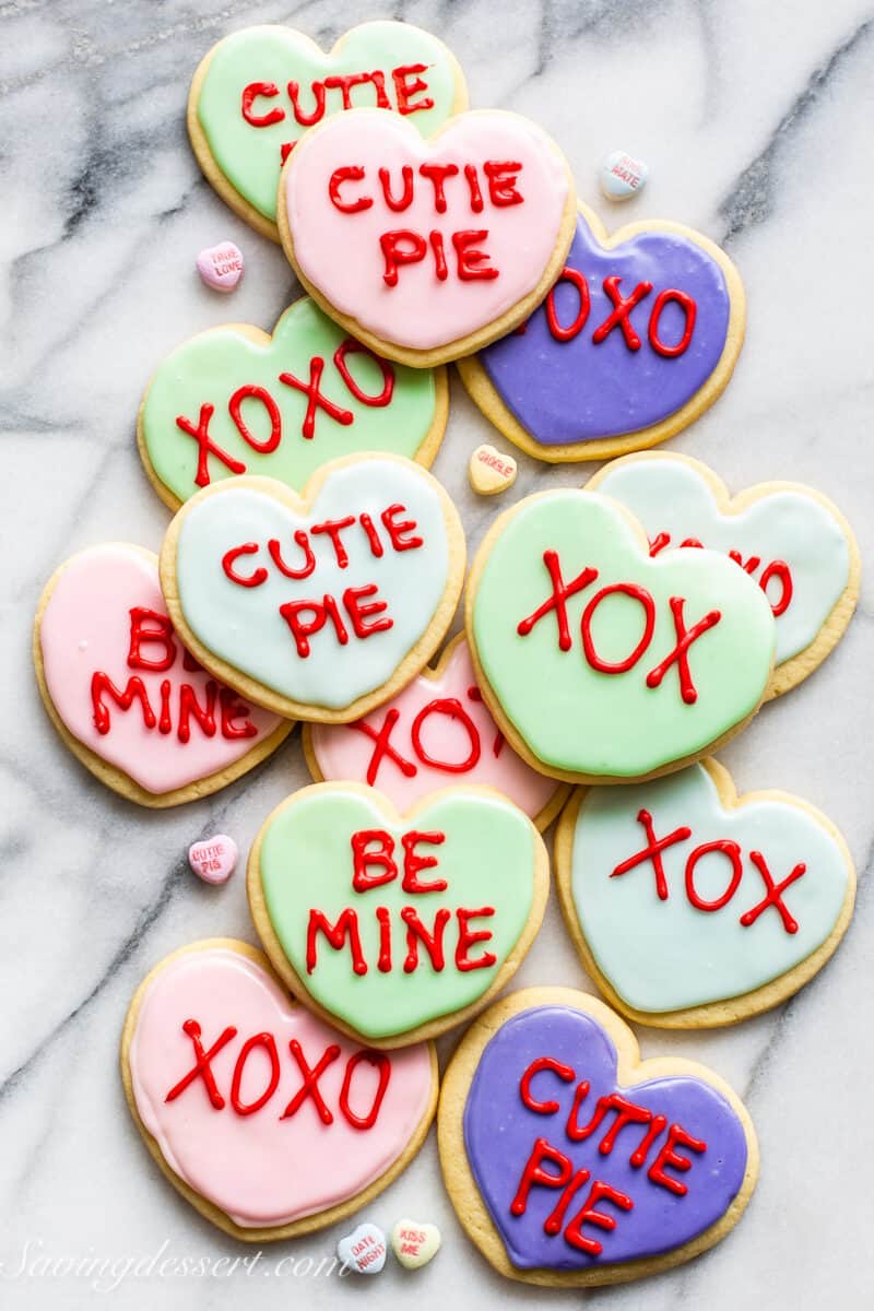 An overhead shot of heart shaped cookies iced with pastel colors with text in red mimicking conversation heart candies.