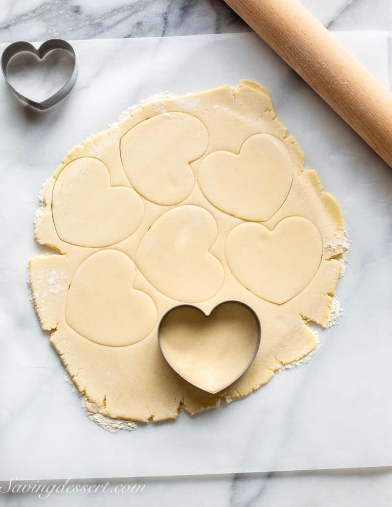 A rolled out round of sugar cookie dough being cut into heart shapes.