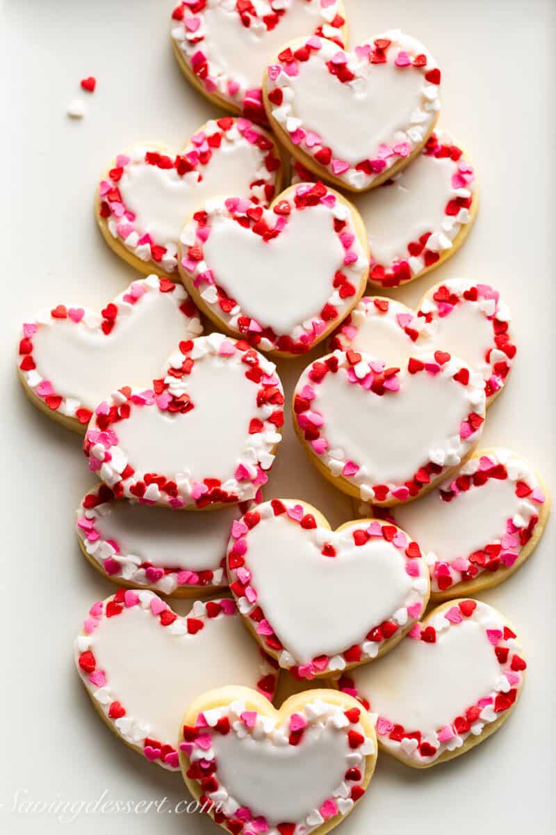 Small heart shaped cookies with white icing and the edges decorated with heart shaped sprinkles.