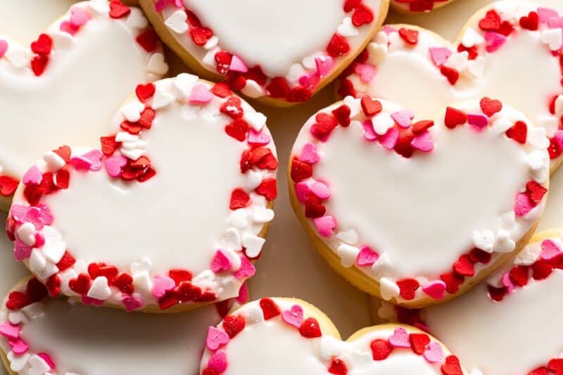 An overhead view of heart shaped cookies decorated with white icing and trimmed with heart shaped sprinkles.