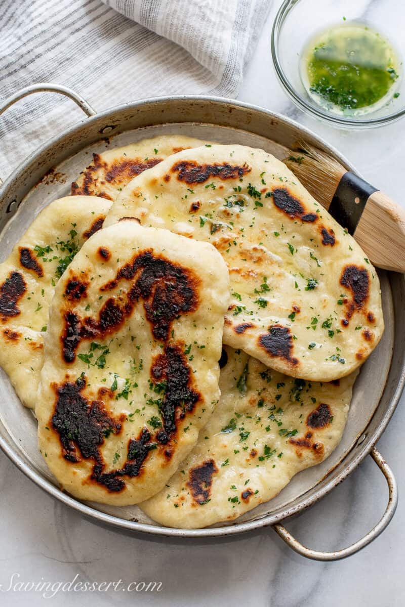 Fresh homemade naan bread rounds in a pan brushed with melted butter with parsley.
