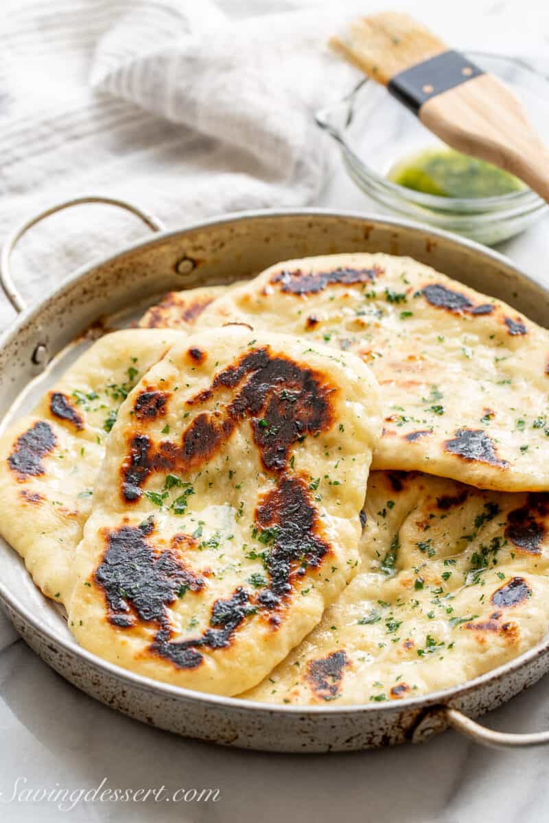 Naan bread stacked in a pan brushed with melted butter and sprinkled with parsley.