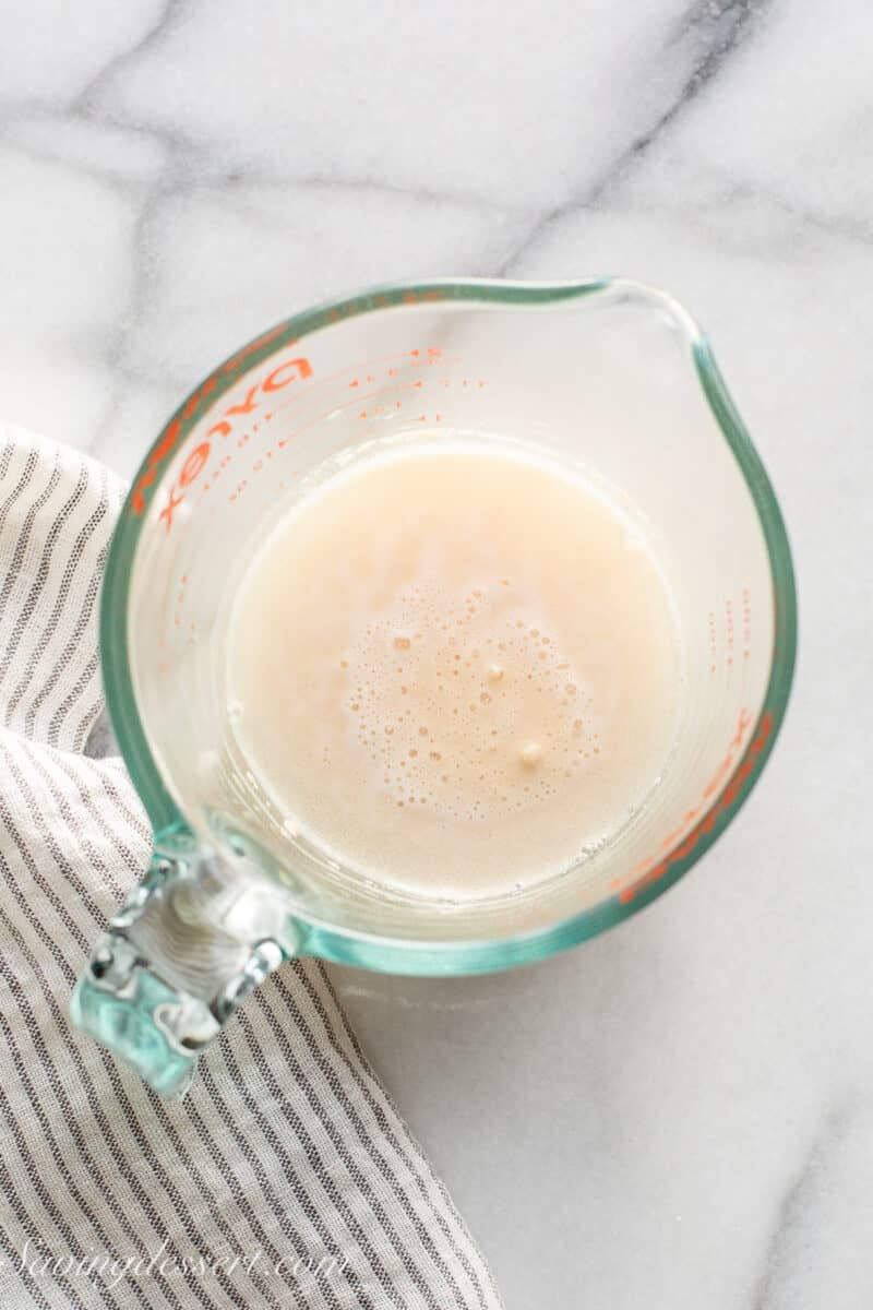 Yeast being dissolved in warm water in a small measuring cup.