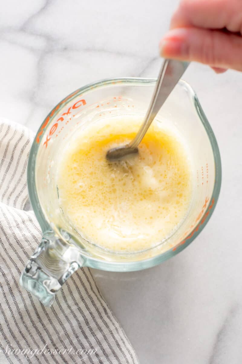 A measuring cup with an egg yolk, oil and milk being combined with a fork.