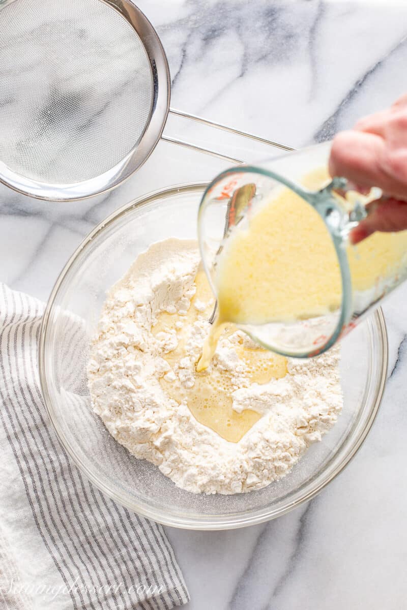 A bowl of flour with a milk, oil and egg mixture being poured into the flour.