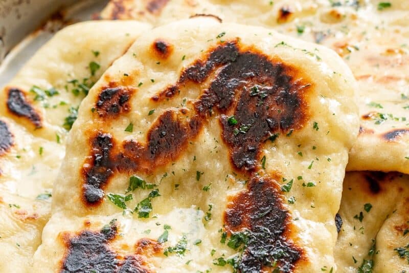 A side view of a pan filled with homemade naan bread topped with melted butter and parsley.