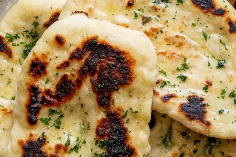 An overhead shot of a pan filled with homemade Naan bread brushed with butter and parsley.