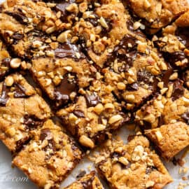 Peanut Butter Blondies cut into squares garnished with dark chocolate and chopped roasted peanuts.