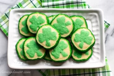 An overhead view of a platter of slice and bake cookies with green clovers in the middle and green sanding sugar around the edges.