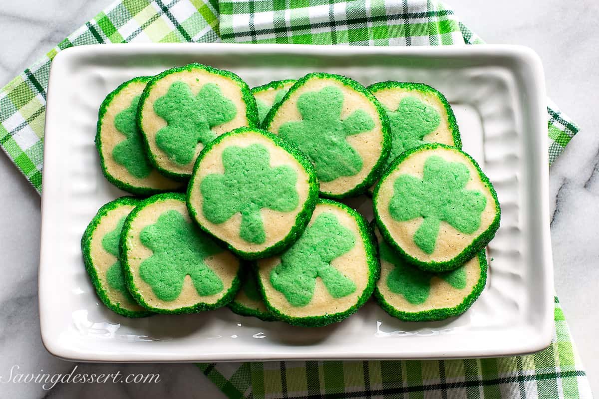 An overhead view of a platter of slice and bake cookies with green clovers in the middle and green sanding sugar around the edges.