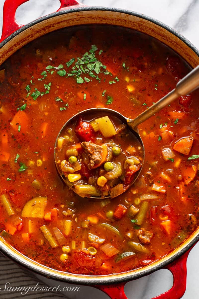 An overhead photo of a big Dutch oven filled with vegetable beef soup topped with fresh parsley.