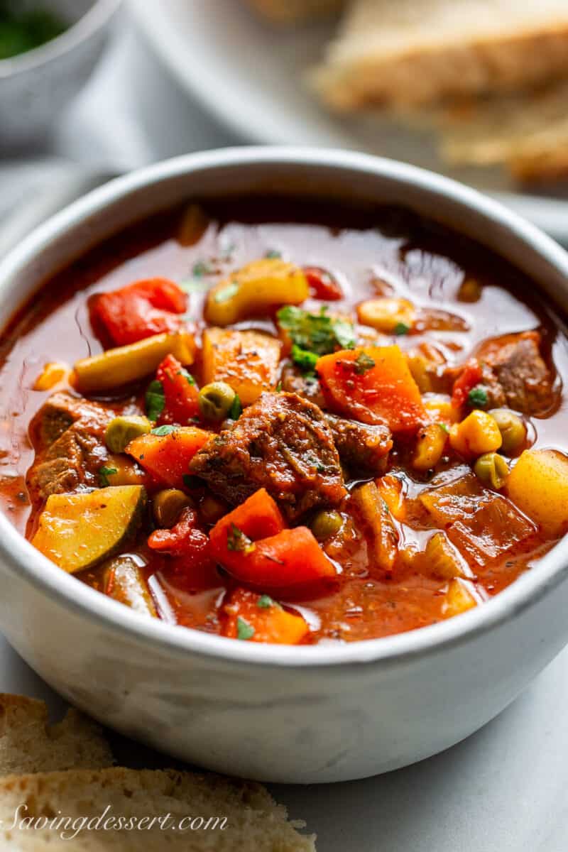 A bowl of chunky soup in a bowl with carrots, celery, beef cubes and potatoes in a rich tomato broth.