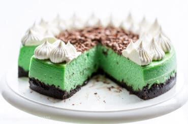 A side view of a sliced grasshopper cheesecake topped with whipped cream and chocolate curls.