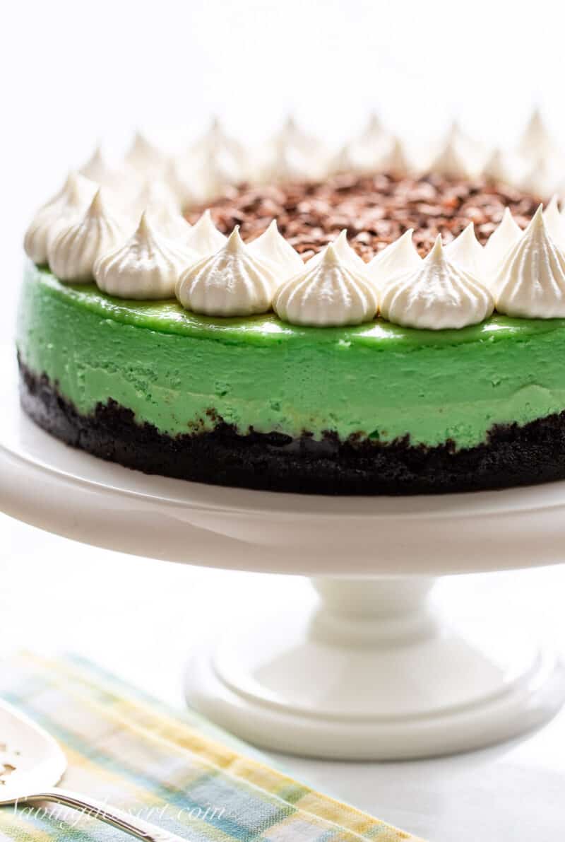 A side view of a whole light green grasshopper cheesecake on a cake stand.
