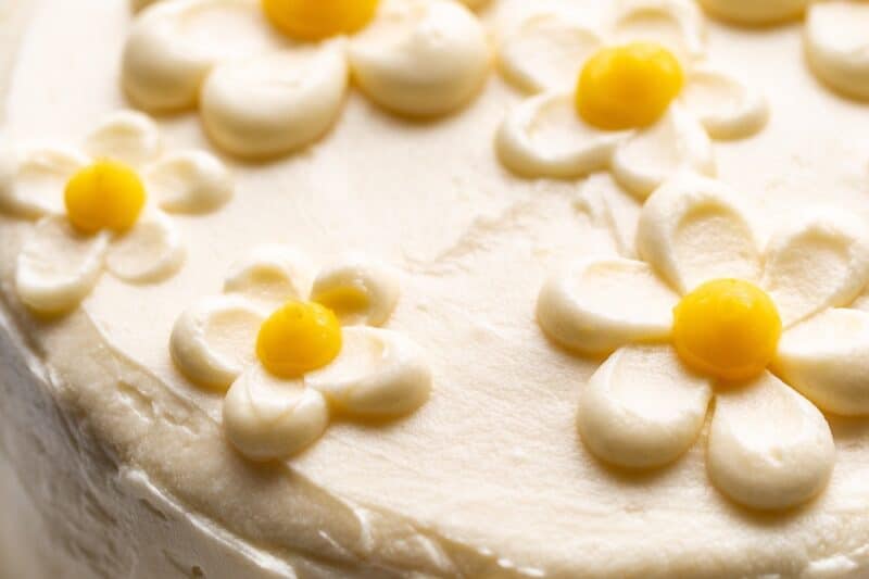 A side view of a whole lemon curd cake topped with pretty buttercream flowers.