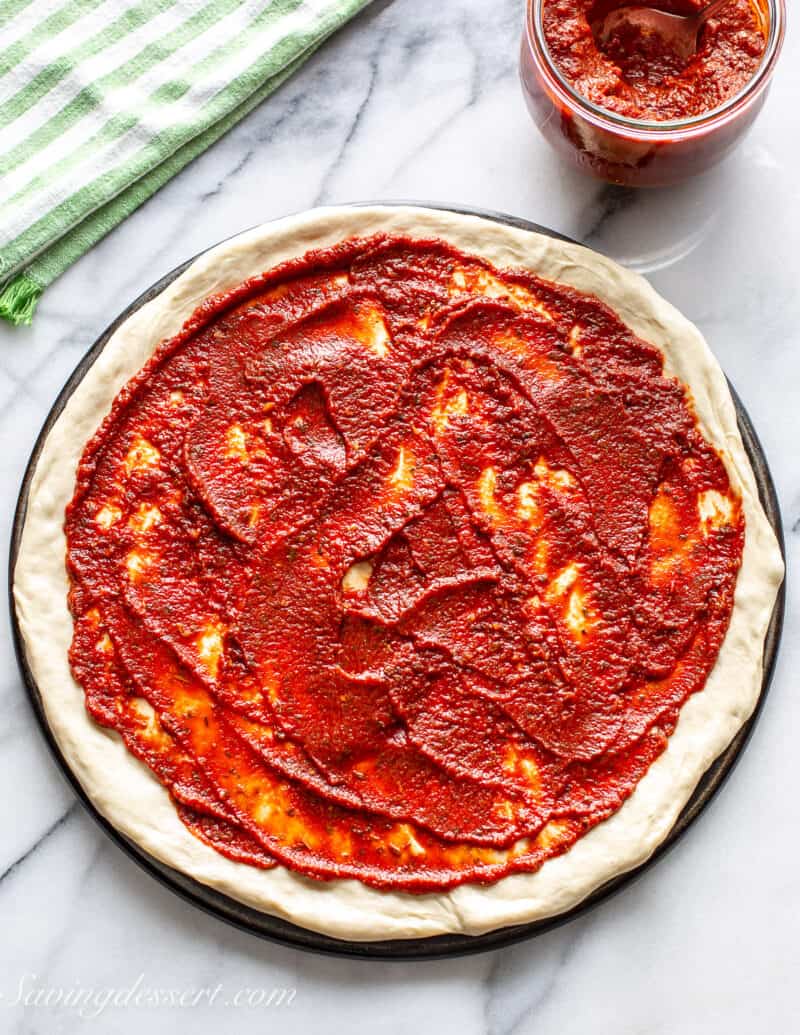 An overhead shot of pizza dough topped with red pizza sauce.