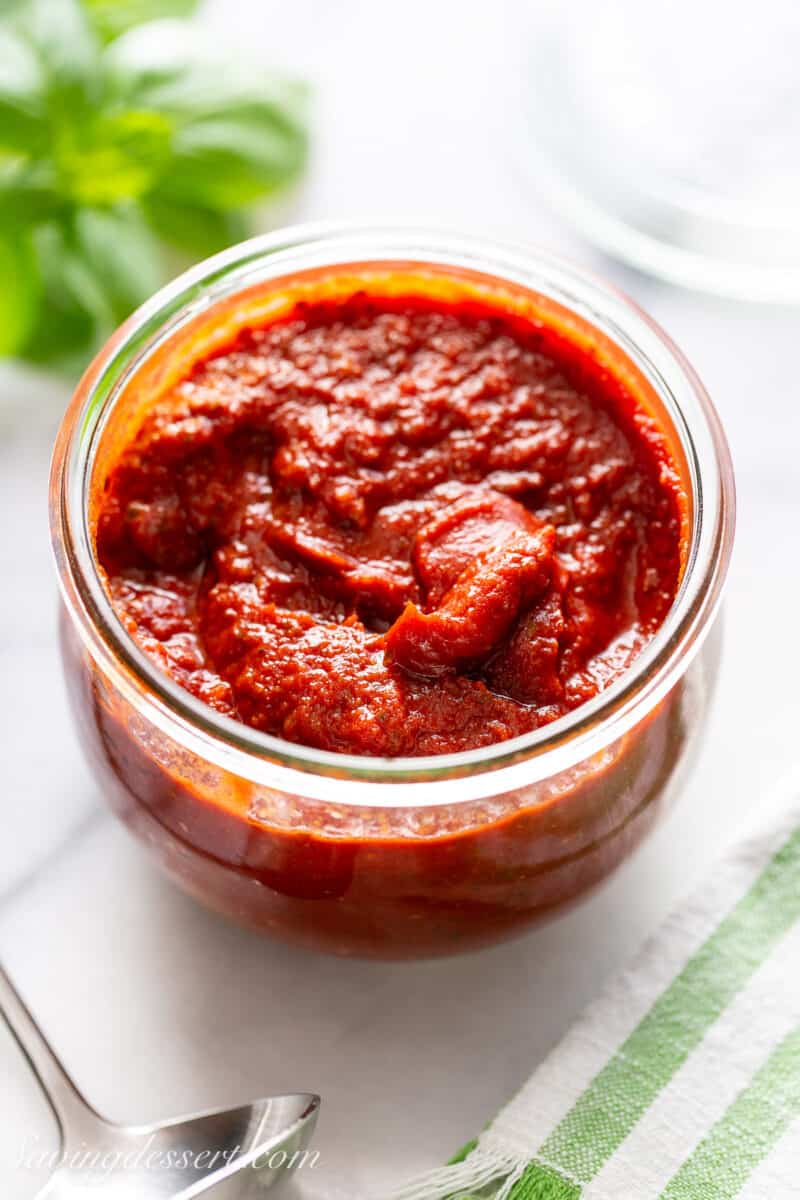 Homemade pizza sauce in a jar with basil on the side.
