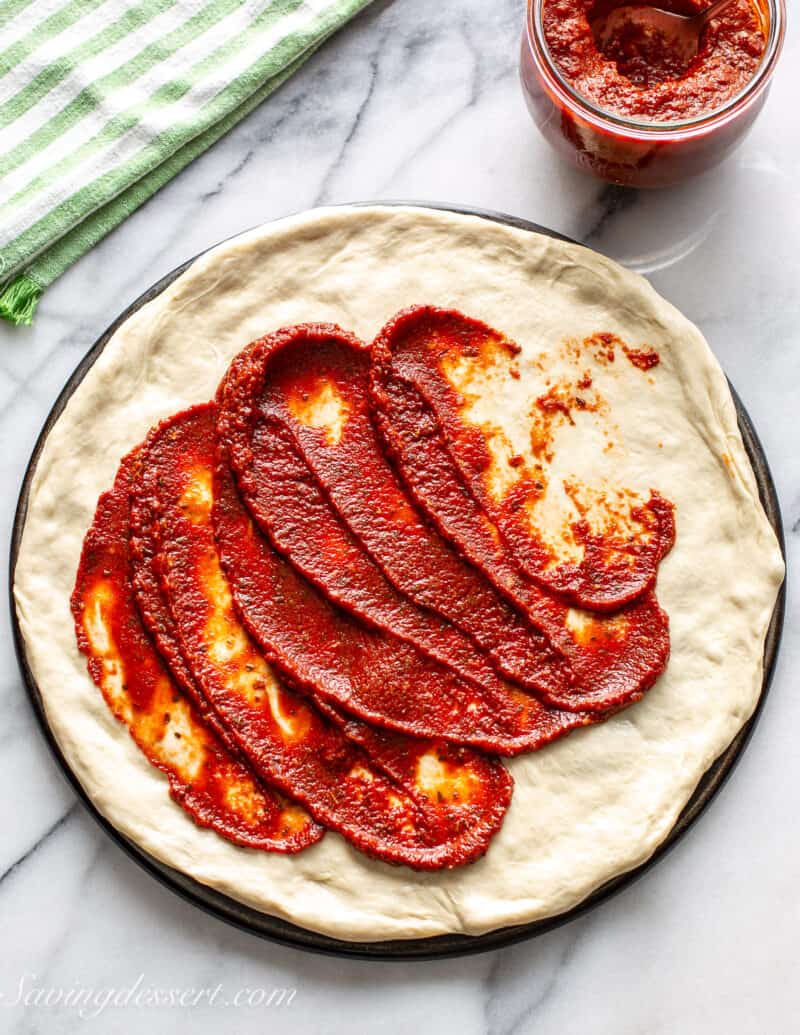 Pizza sauce being spread over an unbaked pizza crust.