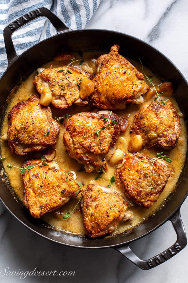 A black skillet filled with crispy chicken thighs in a garlic wine sauce.
