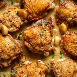 Chicken thighs in a skillet filled with 40 cloves of garlic in a buttery wine sauce.