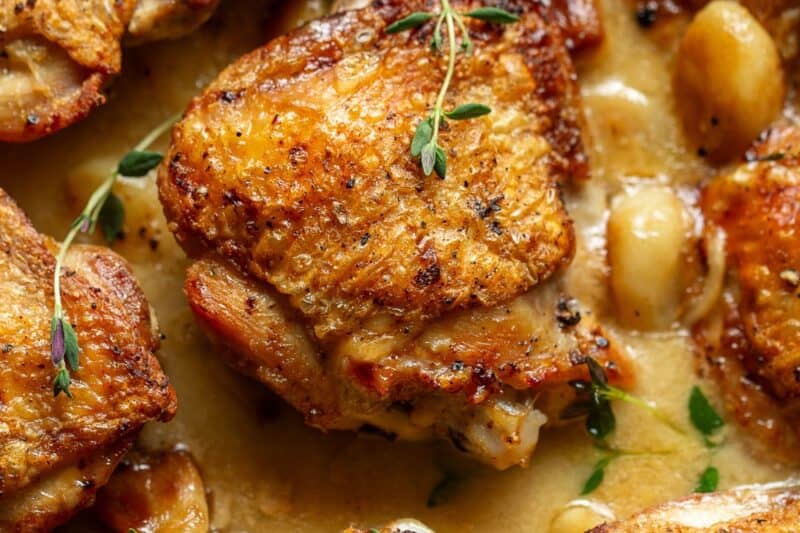 Crispy chicken thighs in a skillet filled with 40 cloves of garlic and a wine sauce with thyme.