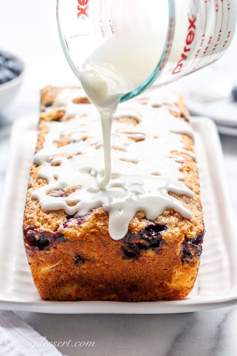 A loaf of blueberry bread being drizzled with lemon icing.