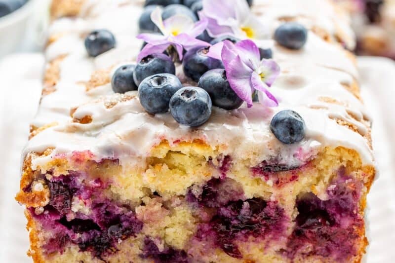 A side view of a sliced blueberry lemon bread topped with blueberries and a lemon icing.