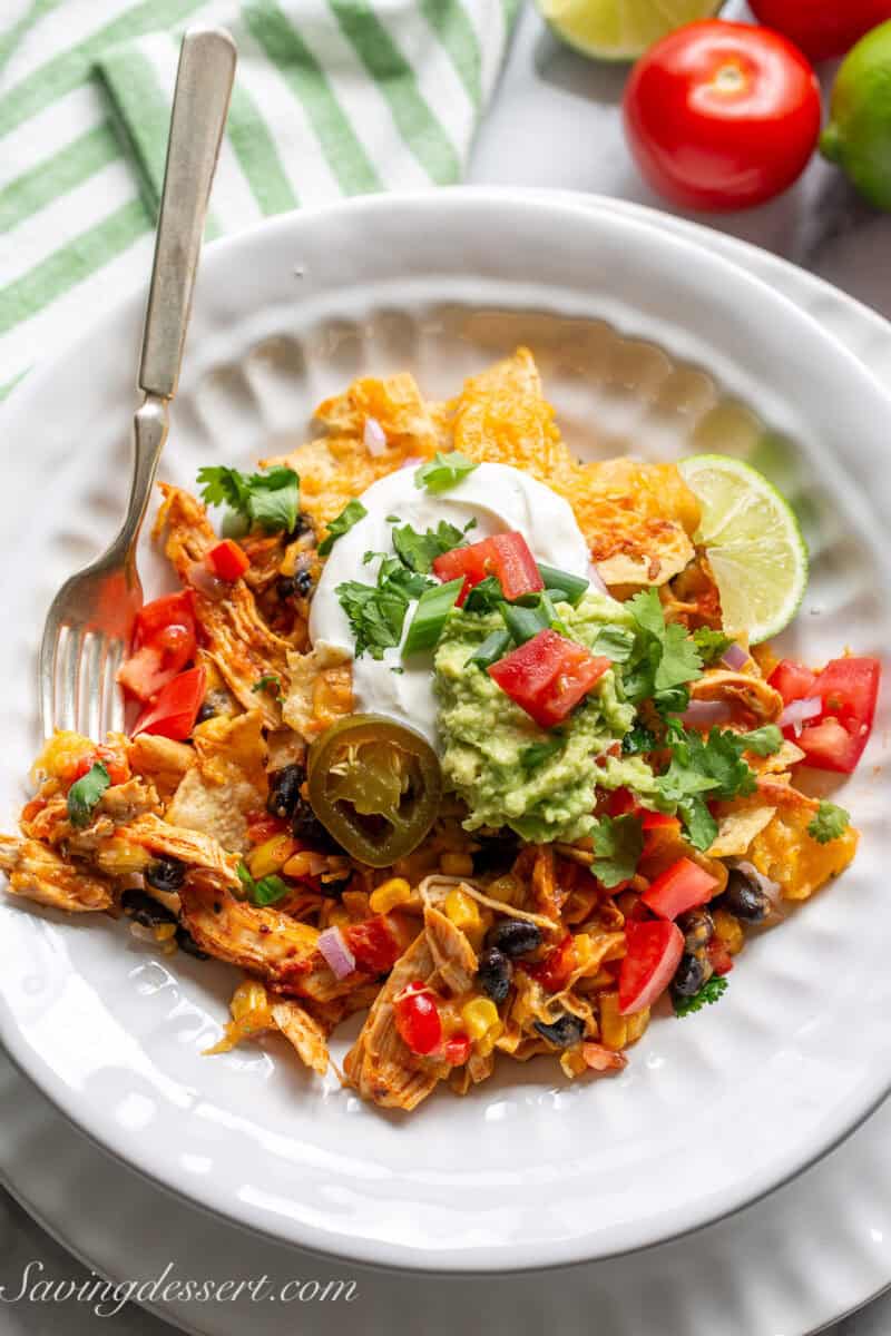 A bowl filled with a chicken taco casserole topped with guacamole, sour cream and tomatoes.