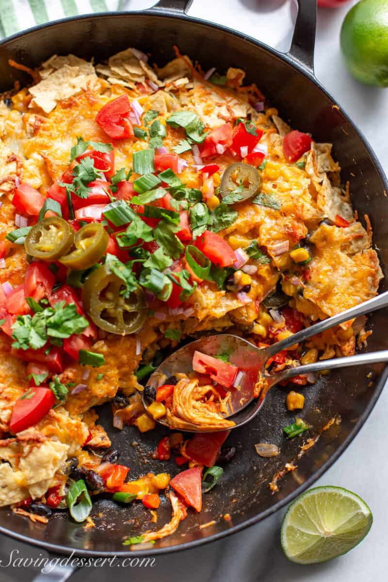 A skillet with spoons of chicken taco casserole being scooped out.