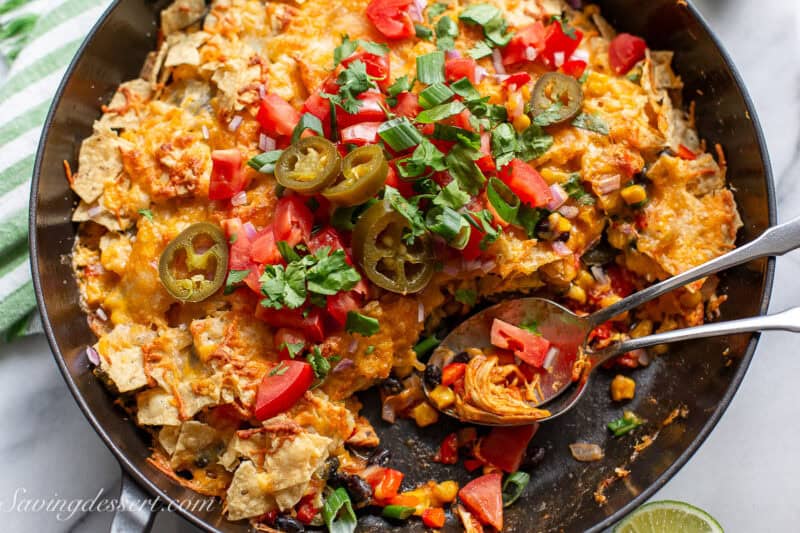 A closeup photo of a skillet filled with chicken taco casserole topped with sliced green onions, tomatoes and chips.