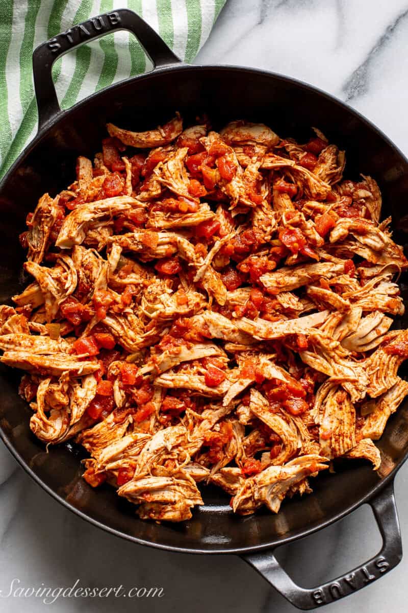 A skillet filled with shredded chicken tossed in taco seasoning and blended with canned tomatoes.