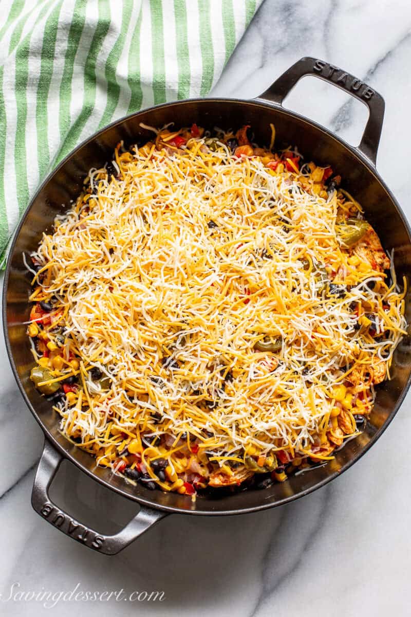 A skillet with chicken taco cassoulet topped with cheese ready to go in the oven.