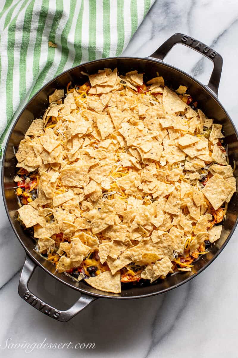 A cast iron skillet filled with chicken taco casserole topped with crumbled chips