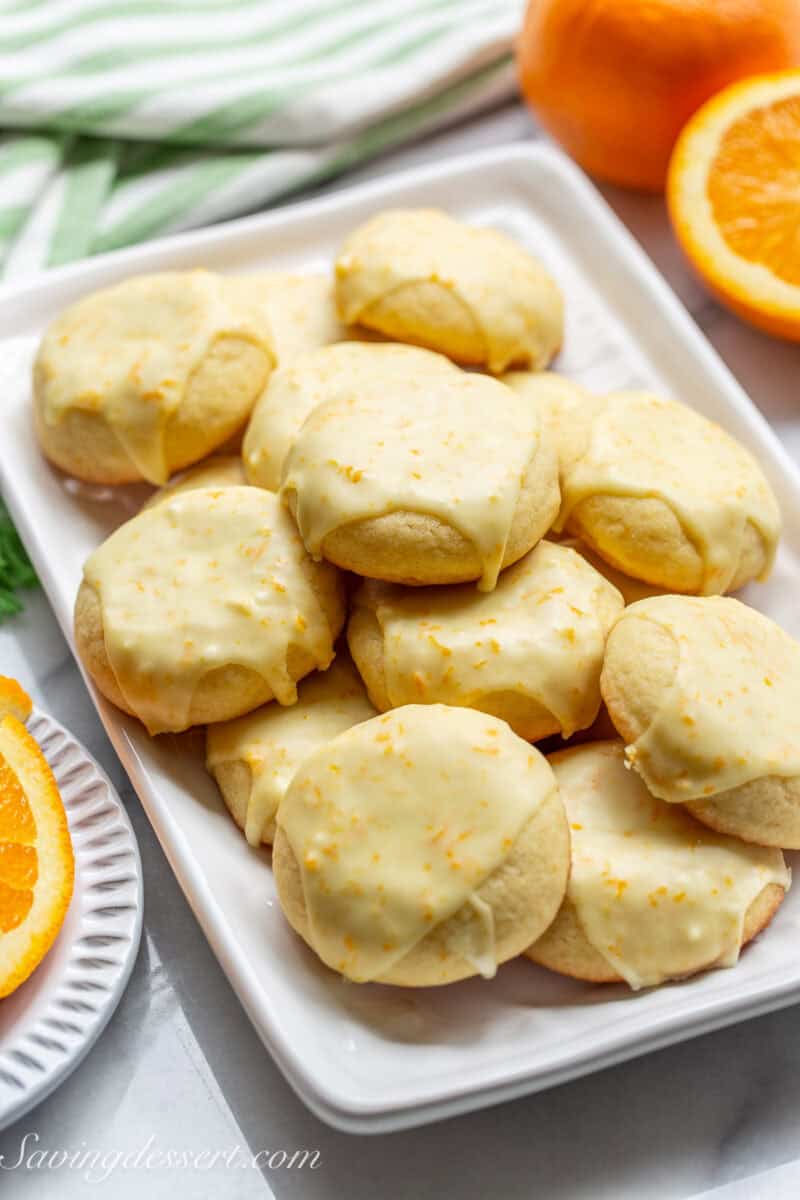 A side view of a platter of iced orange cookies with a sliced orange in the background.