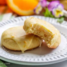 Two orange cookies on a plate with one missing a bite.