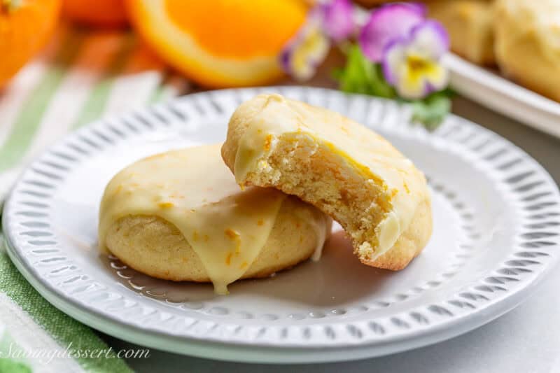 Two orange cookies on a plate with one missing a bite.