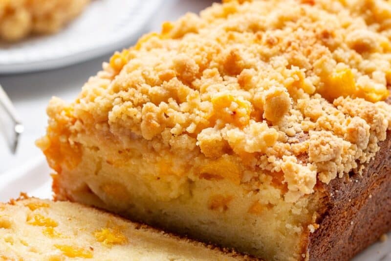 A sliced peach cobbler pound cake on a platter with a sliced peach in the background.
