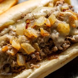 A closeup of a steak sandwich topped with cooked onions.