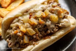 A closeup of a steak sandwich topped with cooked onions.