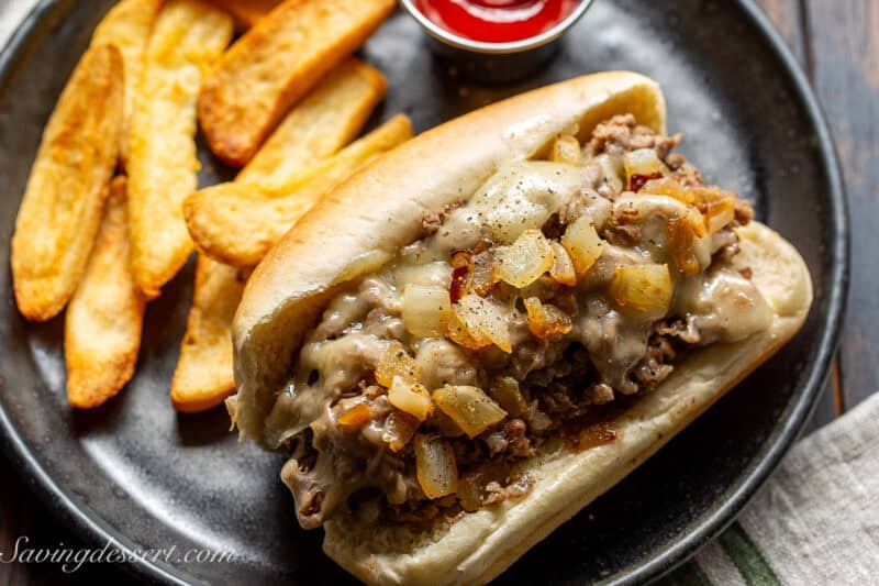 A steak sandwich on a black plate served with french fries and ketchup.
