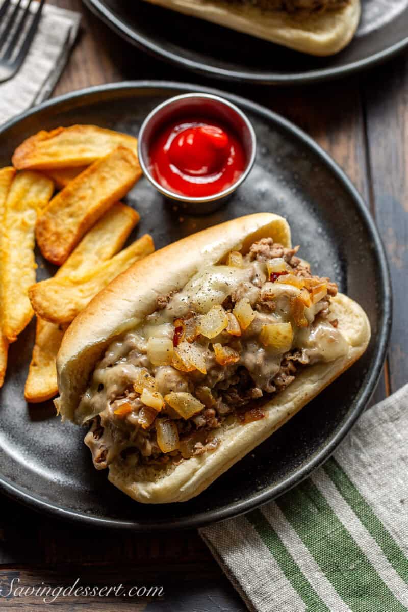 An overhead shot of a steak sandwich topped with caramelized onions and served with french fries and ketchup.