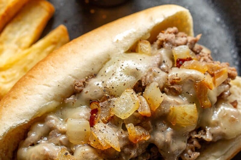 An overhead view of a steak sandwich topped with cheese and onions with french fries and ketchup on the side.