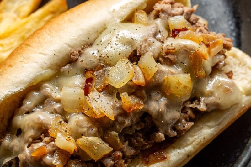 An overhead view of a sub roll filled with steak and cheese with French fries and ketchup on the side.