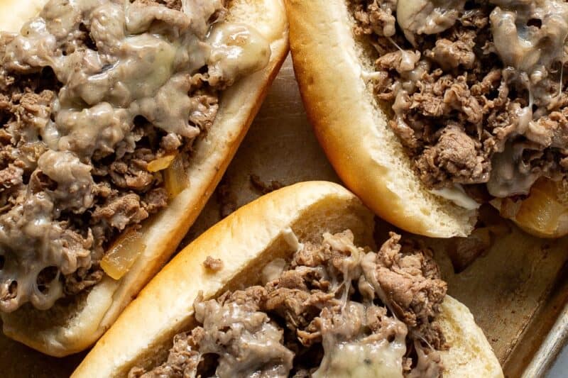 A baking tray topped with three steak and cheese sandwiches.
