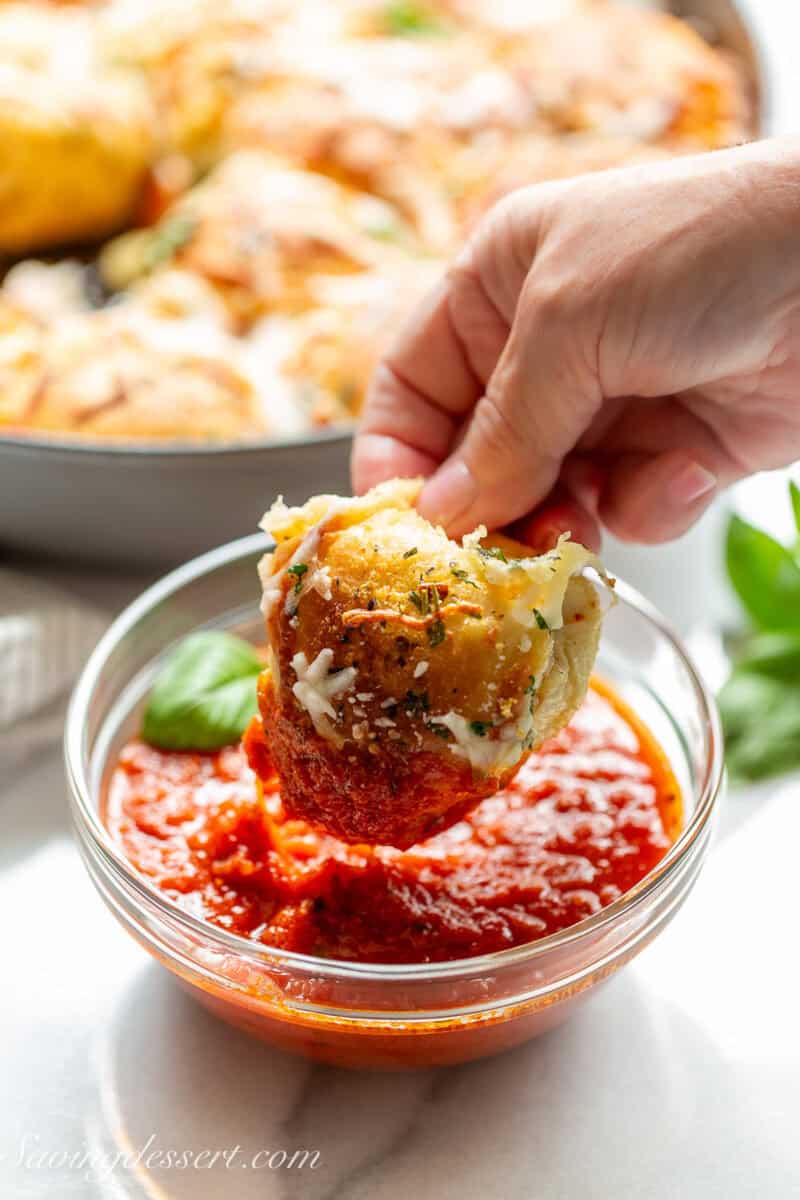 A cheesy roll being dipped in a bowl of pizza sauce.
