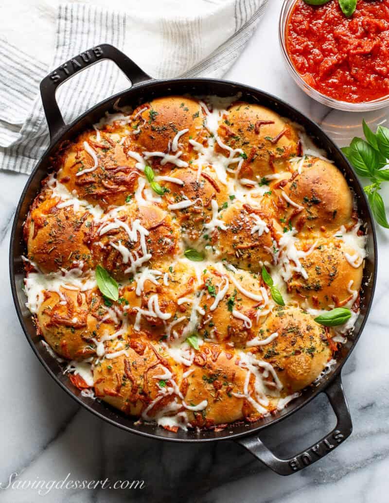 A skillet filled with pizza rolls with mozzarella and pepperoni with pizza sauce on the side.