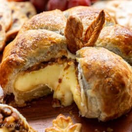 A sliced baked brie in the shape of a pumpkin with warm cheese oozing out of the pastry.