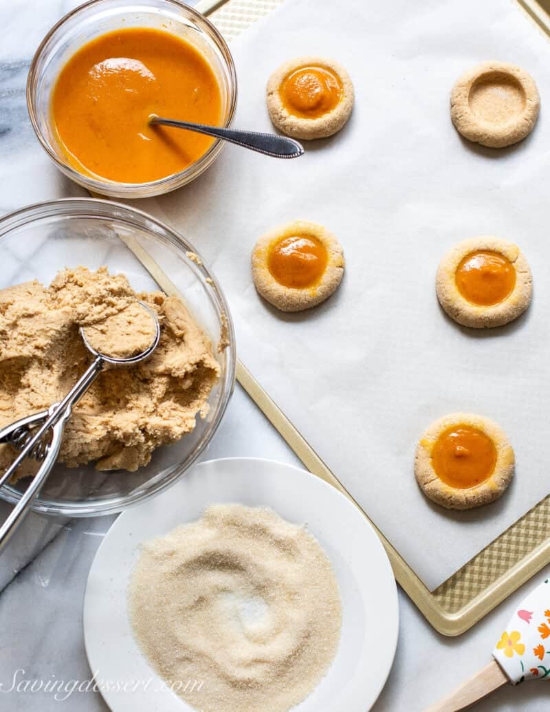An overhead shot of cookie dough in a bowl, coarse sugar for rolling the dough balls and a bowl of pumpkin pie filling.